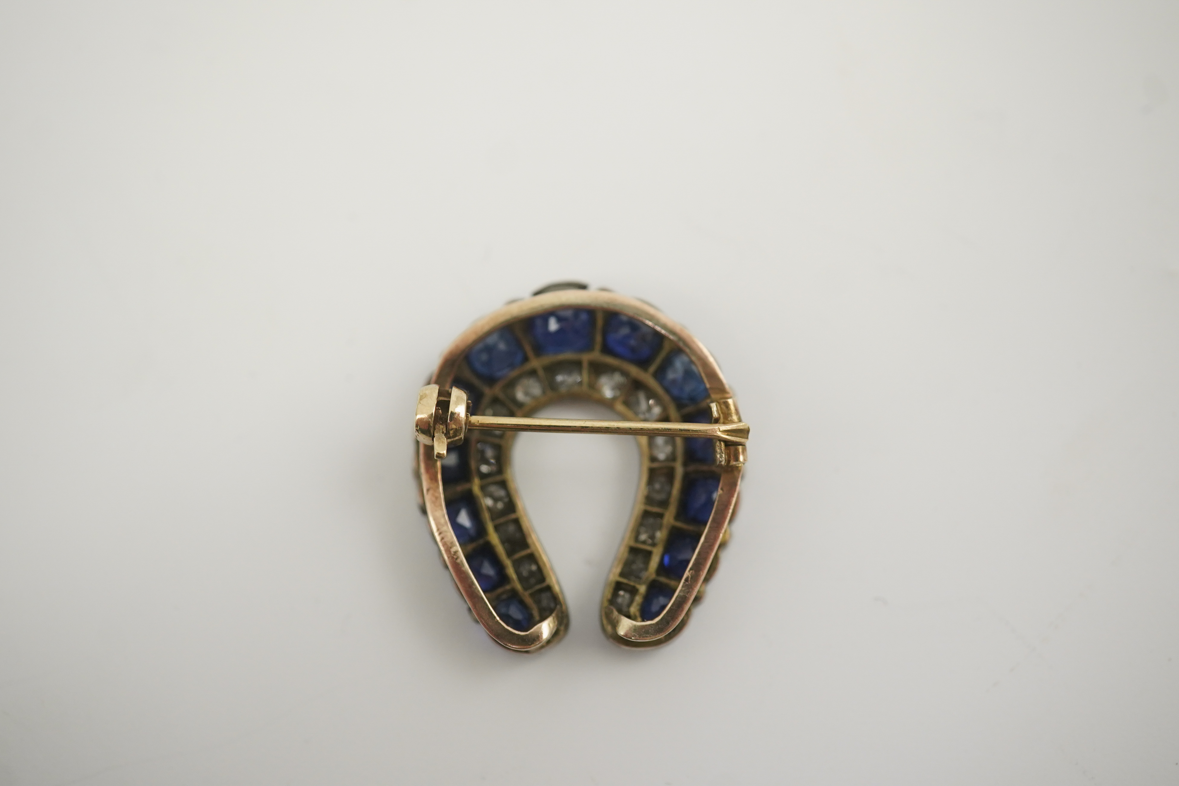 An Edwardian, gold and silver, diamond and sapphire set ‘horse shoe’ brooch